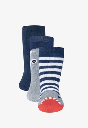 Trois paires de chaussettes : bleu marine, gris avec un motif de requin, et rayures bleu marine/blanc, avec une bouche de requin rouge sur le bout. Texture en maille douce.