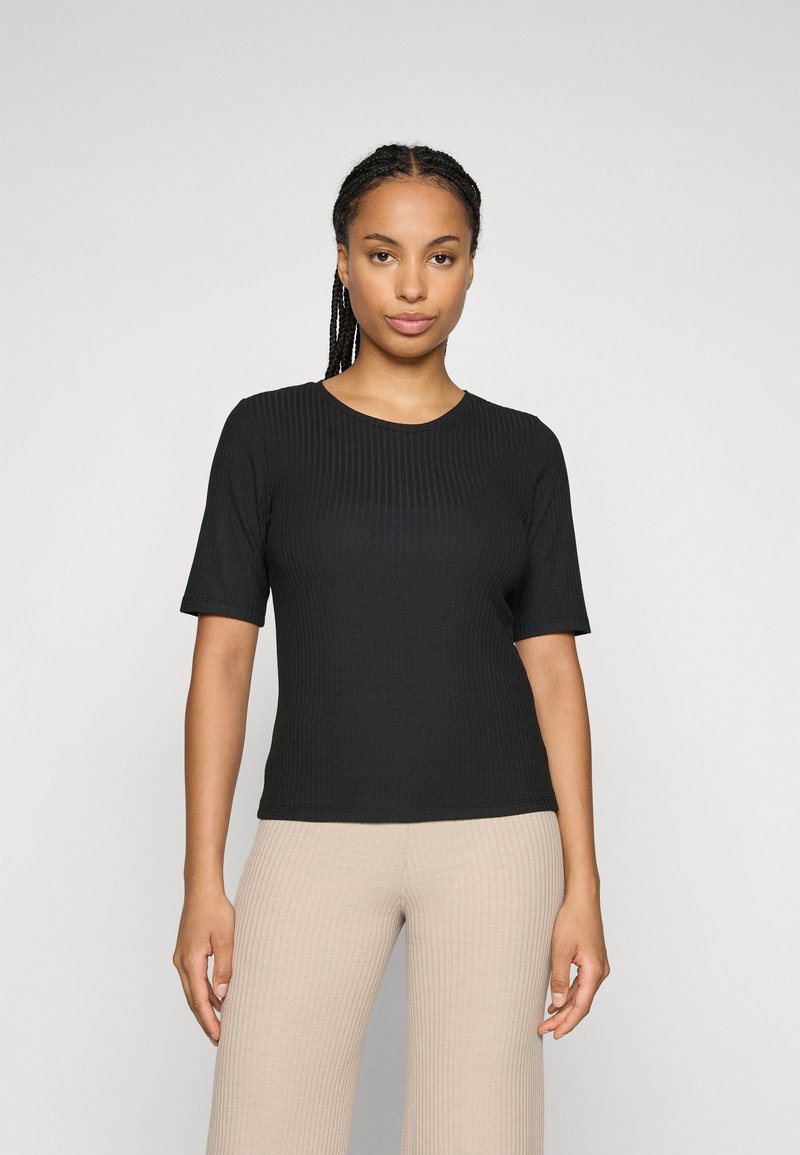 Black ribbed short-sleeve top with a round neckline, fitted design, and smooth texture. Worn with beige ribbed high-waisted pants.