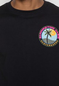 Schwarzes Baumwoll-T-Shirt mit einem kreisförmigen Grafikdesign, das eine Palmen, die Sonne und den Text "SUMMERTIME OASIS SCOTCH&SODA" in leuchtenden Farben zeigt.