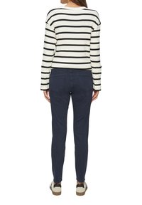 Pull léger rayé crème et noir porté avec un pantalon slim-fit bleu marine. Caractéristiques : texture côtelée et chaussures décontractées avec des accents noirs.