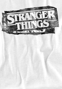 Weißes T-Shirt mit einem verwaschenen schwarzen Grafiklogo, auf dem "STRANGER THINGS" in fetten, Großbuchstaben steht.