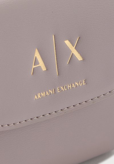 Gros plan sur un cuir beige avec le logo Armani Exchange embossé en or et des détails de couture visibles.