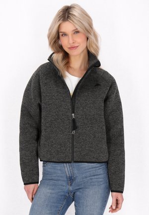 Harmaa fleece-takki, jossa on vetoketjulla varustettu etuosa, korkea kaulus ja mustat yksityiskohdat. Takki riderä mukautuva malli ja karkea kangas. Päällä valkoinen paita.