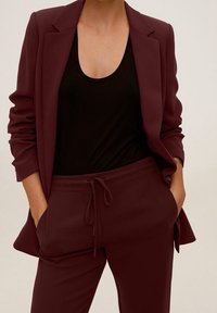 Blazer bordeaux cintré porté sur un débardeur noir, associé à un jogging bordeaux assorti avec une taille élastique et un cordon de serrage.