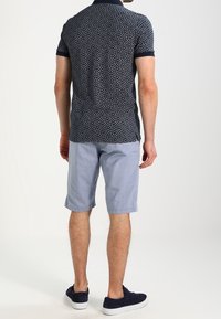 Granatowa koszulka polo z małym białym kwiatowym wzorem, zestawiona z jasnoniebieskimi szortami. Koszulka ma kołnierzyk i kontrastowe mankiety. Białe trampki.