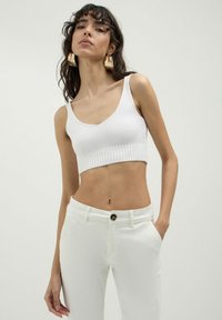Top corto a costine bianco con scollatura rotonda, indossato con jeans bianchi aderenti dotati di chiusura con bottone e tasche laterali.