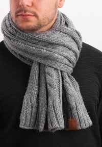 Knitted gray scarf with a textured, cable pattern. Features a leather accent tag. Worn loosely around the neck.