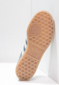 Blue suede sneaker sole with a patterned rubber outsole, featuring a circular emblem and three white stripes across the side.