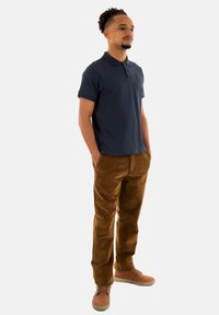 Mörkblå pikétröja med kort ärm, texturerad tyg; kombinerad med bruna kordbyxor. Ljusbruna skor fulländar outfiten.