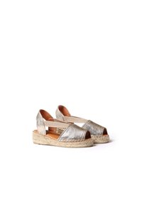 Metalické strieborné espadrilky so otvorenou špičkou, elastickými krížovými popruhmi a tkanými jútovými stredovými podrážkami. Plochý dizajn po členky vhodný na bežné nosenie.