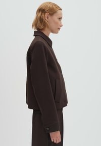 Bruine cropped jas met kraag, knoopsluiting en zijzakken. Gemaakt van gestructureerde stof met een gladde afwerking.