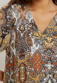 Färgglad blus med V-ringning, med intrikata paisleymönster i orange, brunt, kräm och rosa på ett lätt tyg.