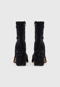 Botine negre din suede cu detalii decorative din ținte argintii, închidere cu fermoar și toc înalt pătrat. Caracteristici include o textură fină și un design bine adaptat.