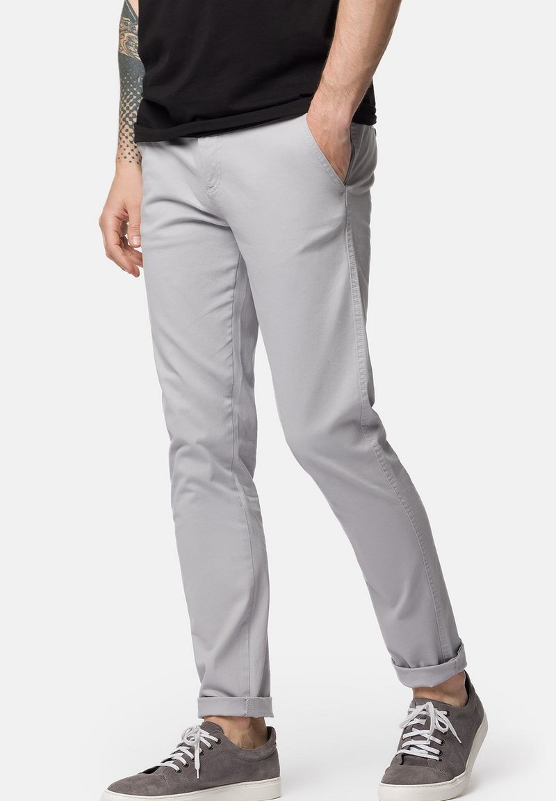 Jasnoszare chinos o tapered fit, z bocznymi kieszeniami i podwiniętymi mankietami. Noszone z szarymi sneakersami, które mają subtelną fakturę.