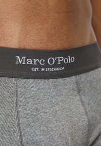 Grå ribbad tygboxer med en svart midjeband som har "Marc O'Polo"-logotypen och "EST. I STOCKHOLM" i vita bokstäver.