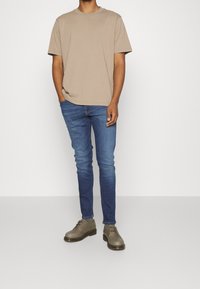 Krátký rukáv béžový tričko s kulatým výstřihem, kombinované s tmavě modrými slim-fit džíny a šedými šněrovac ími botami s tlustou černou podrážkou.