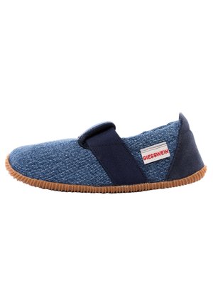 Bottine en denim bleu à enfiler avec une semelle en caoutchouc, une sangle élastique, un tissu texturé et des détails en accent tan. Possède une étiquette logo sur le côté.