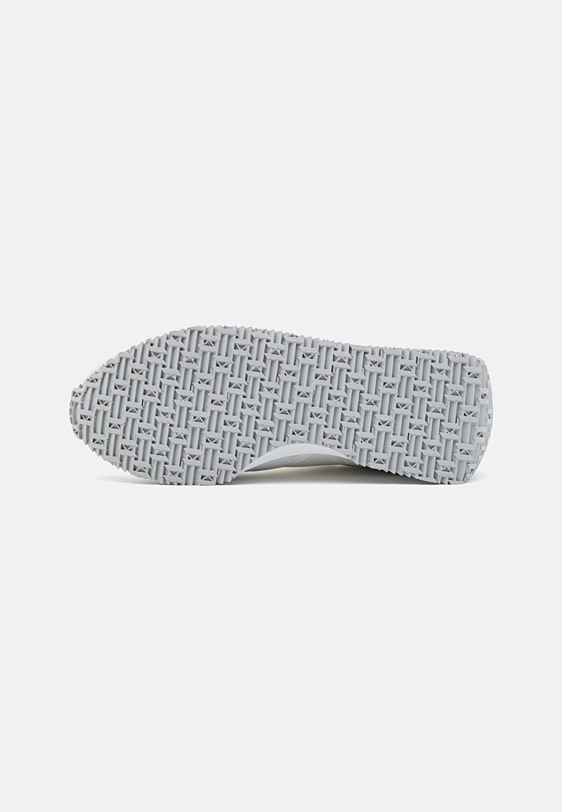Suela de sneaker gris con una superficie de goma texturizada que presenta un patrón geométrico. El diseño incluye un talón redondeado y una banda de rodadura resistente.
