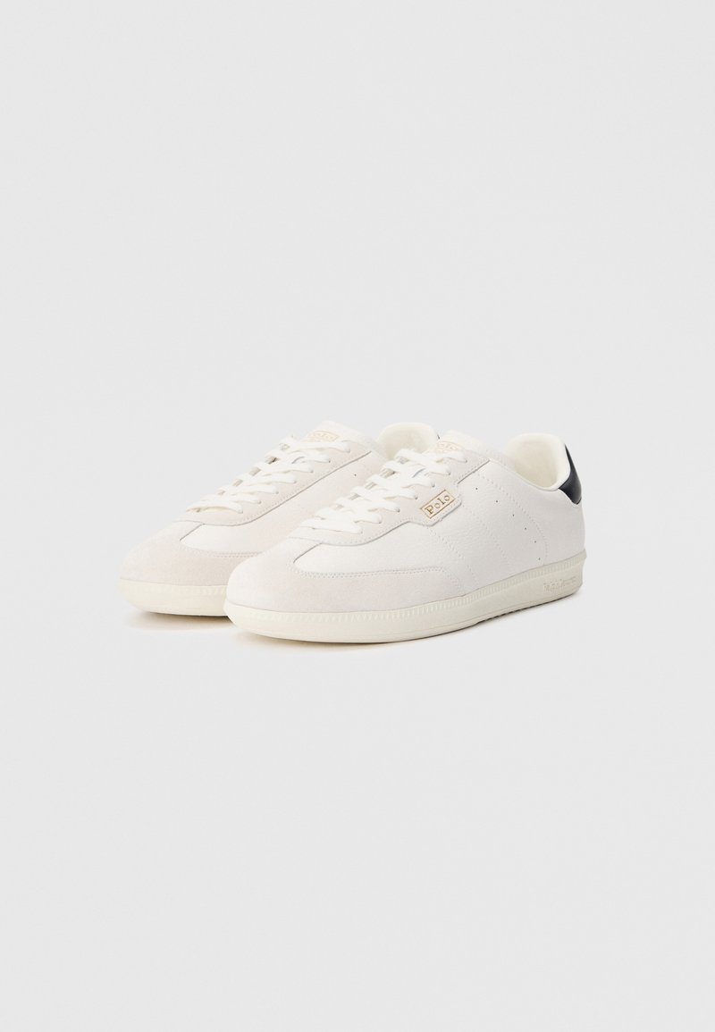 Sneakers in suede bianco con finitura liscia, caratterizzate da un inserto nero sul tallone, dettagli beige e un classico design con lacci.