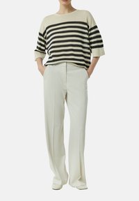 Sweter w paski w odcieniach beżu i czerni, luźny krój z krótkimi rękawami; połączony z szerokimi spodniami w kolorze kremowym, gładka tekstura i dopasowany krój.