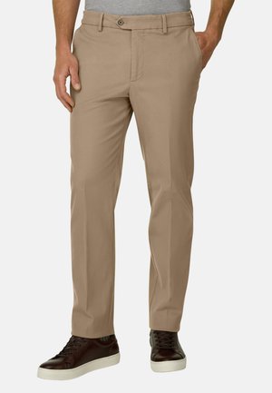 Homme portant un pantalon beige droit avec poches latérales et arrière, associé à des baskets basses marron foncé avec semelles blanches.