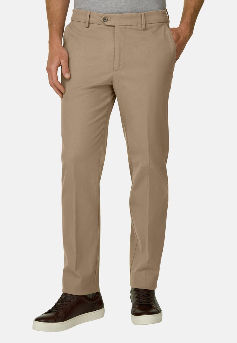 Homme portant un pantalon beige droit avec poches latérales et arrière, associé à des baskets basses marron foncé avec semelles blanches.