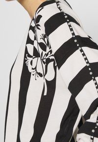 Czarny i biały sweter w paski z kwiecistym wzorem z jednej strony, ozdobiony dekoracyjnymi ćwiekami wzdłuż szwu rękawa.