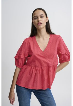 Blouse rose corail avec un décolleté en V profond, des manches bouffantes et des accents froncés. Le matériau présente une texture à petits pois subtile ; forme évasée à la taille.