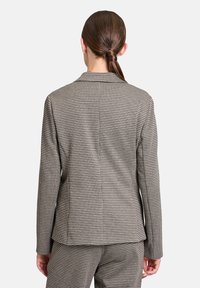 Blazer à motif pied-de-poule en marron et crème, avec une coupe ajustée, des revers crantés et une texture lisse avec des épaules structurées.