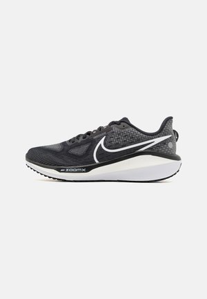 Chaussure de sport noire avec une tige en maille dotée de motifs texturés, des accents blancs, une semelle intermédiaire rembourrée et une semelle extérieure en caoutchouc avec une bonne adhérence.