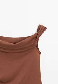 Top senza maniche marrone realizzato in tessuto testurizzato, presenta un design off-shoulder con spalline torcigliate e un morbido scollo drappeggiato.