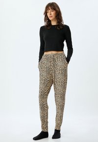Zwarte lange mouwen cropped top gecombineerd met leopardprint tapered broeken met een elastische tailleband en zijzakken. Zwarte sokken.