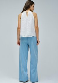 Top bianco senza maniche con texture floreale e schiena a chiave, abbinato a pantaloni larghi blu chiaro. Tessuto morbido e vestibilità rilassata.