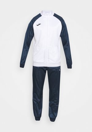 Track suit in white and navy, with a fitted design. Jacket features a high collar and zip; pants are tapered with elastic cuffs.