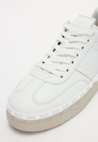 Baskets blanches avec un dessus en cuir lisse, des lacets plats, une languette rembourrée et une semelle en caoutchouc présentant des clous ronds le long du bord.