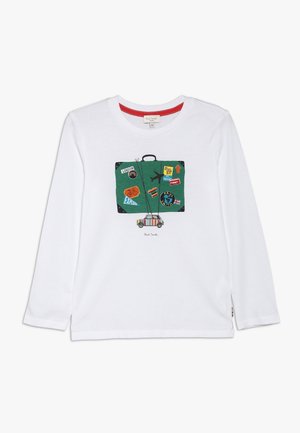 Camisa blanca de manga larga con un gráfico de una maleta verde decorada con pegatinas de viaje, incluyendo "Londres", e ilustraciones de un avión y una bicicleta.