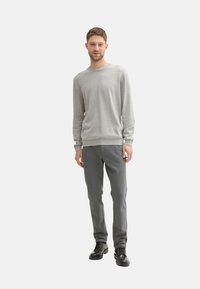 Szary sweter z długim rękawem, wykonany z miękkiego materiału, zestawiony ze slim-fit szarymi spodniami oraz czarnymi sznurowanymi butami. Prosty design, bez wzorów.