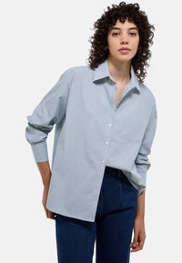 Chemise à rayures bleu clair et blanche, à manches longues et avec une poche sur la poitrine. Fabriquée en tissu léger avec une coupe décontractée.