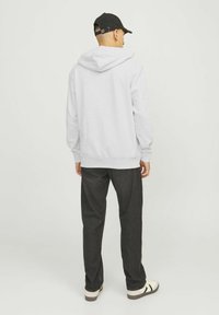 Grauer Hoodie mit Kordelzug, getragen mit dunklen Jeans und weißen Turnschuhen. Die Rückseite des Hoodies hat eine große, weiche Textur.