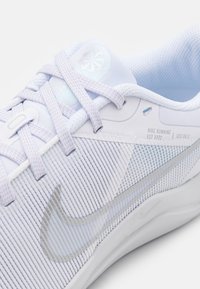 Gros plan sur une chaussure de course Nike bleu clair et blanche avec des lacets, une tige en mesh et un logo, montrant le texte "Nike Running Est 1972" sur le côté.