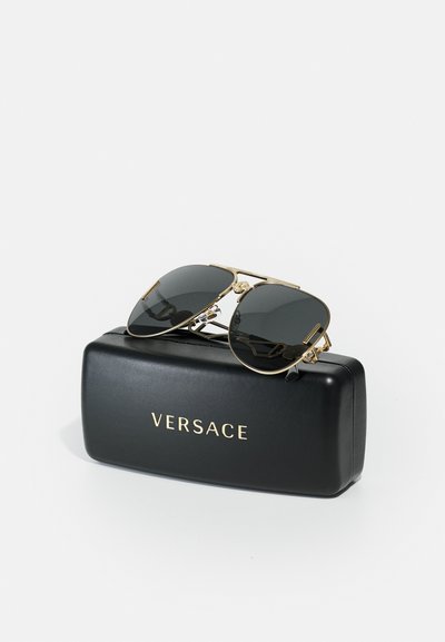 Ochelari de soare Versace negri, cu ramă din metal aurit și lentile întunecate, așezați pe o carcasă neagră ce prezintă logo-ul Versace în aur.