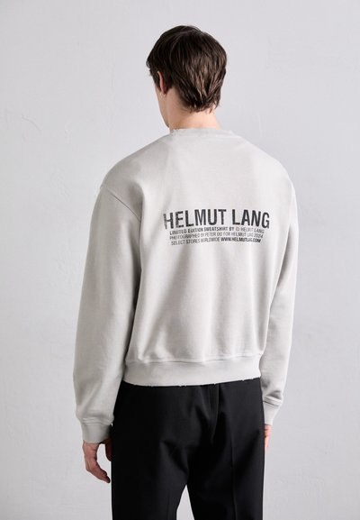 Felpa grigia chiara con collo a giro e polsini a coste. Presenta testo nero sulla parte posteriore, inclusi "HELMUT LANG" e dettagli di design.