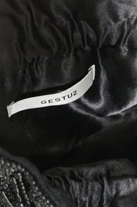 Valge kangast silt, millel on "GESTUZ" tekst, kinnitatud musta läikiva, rüheldatud kangast voodri sisse.