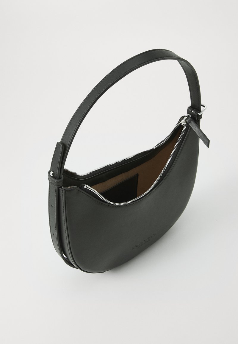 Czarna skórzana torebka o zakrzywionym kształcie, z zamknięciem na zamek i regulowanym paskiem. Wnętrze ma kontrastowe, jasnobrązowe wykończenie.