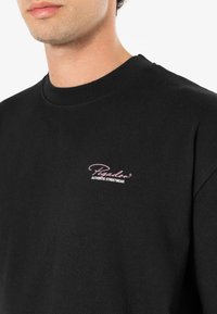 Juodas medvilninis džemperis su apvalia kaklo iškirpte, su mažuoju rožiniu siuvinėtu logotipo užrašu "Pegador AUTHENTIC STREETWEAR."