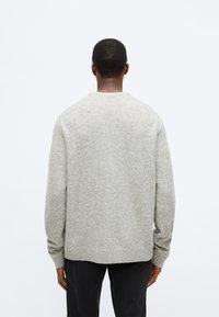 Γκρι πλεκτό πουλόβερ με στρογγυλή λαιμόκοψη, άνετη εφαρμογή και ριμπ μανσέτες. Απαλή υφή με ελάχιστες λεπτομέρειες, συνδυασμένο με σκούρο παντελόνι.