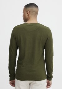 Maslinasto zeleni dugi rukav košulja s okruglim izrezom, s teksturiranim materijalom i prilagođenim dizajnom. Stražnji pogled ističe detalje šavova.