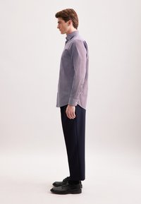 Camicia a fantasia viola chiaro con colletto button-down, abbinata a pantaloni blu scuro e scarpe nere, vista di lato.