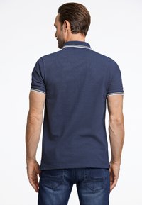 Marinblå pikétröja med texturerad tyg, kontrasterande randiga detaljer vid ärmsluten, korta ärmar och rak nederkant. Bärs med blå jeans.