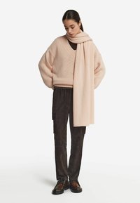 Lys rosa oversized striktrøje med V-hals, parret med mørke cargo bukser og brune snørebåndssko. Inkluderer et matchende langt tørklæde.